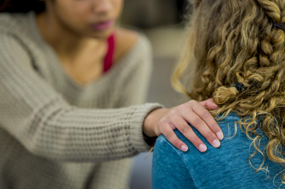 A person places a comforting hand on another person's shoulder, offering support.