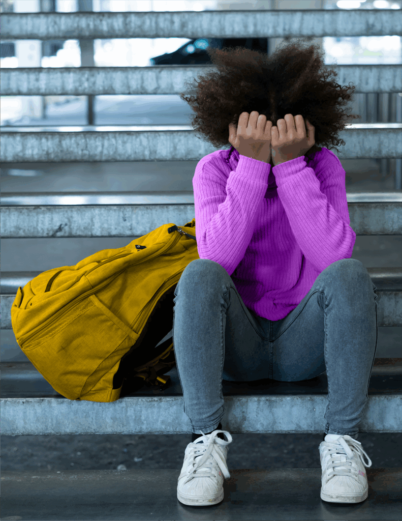 A person in a purple sweater sits on stairs with their head in their hands next to a yellow bag.