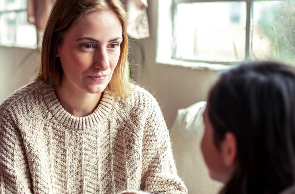 A blonde woman in a white sweater talking to a teen girl.