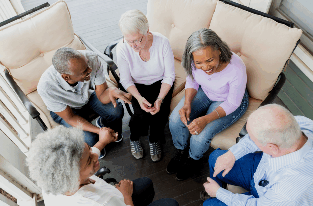 Five adults sit in a circle on a porch, talking and smiling, viewed from above.