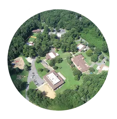 Aerial view of a small campus or residential area surrounded by trees and greenery, with several buildings and roads visible.