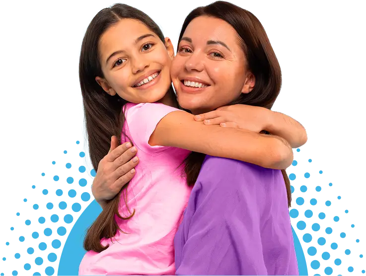 A young girl in a pink shirt hugs an adult woman in a purple top. Both are smiling and looking at the camera.