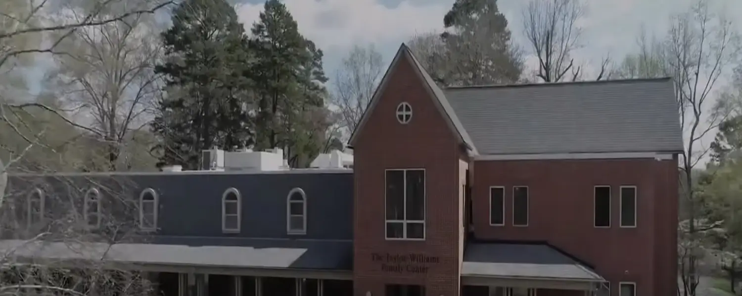 A two-story red brick building with a peaked roof, surrounded by trees. The sign on the building reads "The Judge William Family Center.