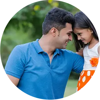 A man wearing a blue polo shirt smiles and leans his forehead against a young girl in an orange polka dot skirt outdoors.