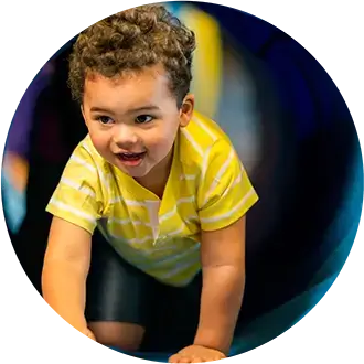 Young child with curly hair wearing a yellow striped shirt is crawling on hands and knees, looking forward and smiling.