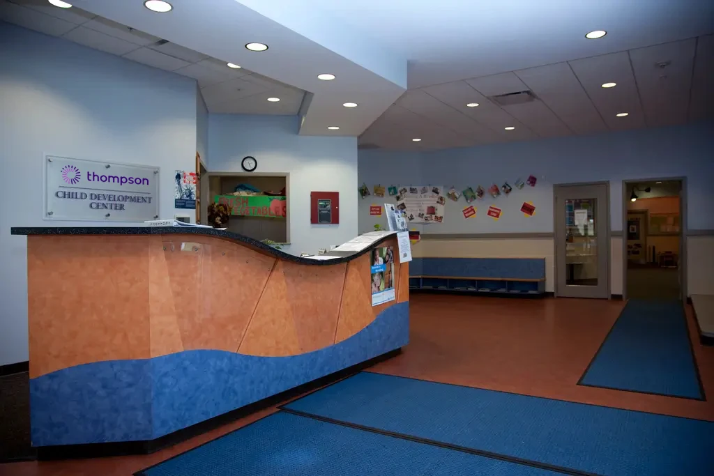 Reception area of the Thompson Child Development Center with a curved desk, blue mats, bulletin board, and children's artwork displayed on the back wall.