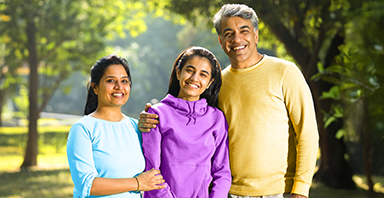 Three people, two adults and one teenager, stand outdoors in a park, smiling at the camera. With trees in the background, they embody the spirit of prevention—Thompson Child and Family Focus is dedicated to creating brighter futures like theirs.