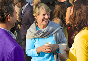 A woman in a blue top holds a cup and smiles while discussing her journey to becoming a Partner at Thompson Child and Family Focus with two people at an outdoor gathering.